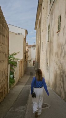 Mallorca 'nın eski kasabasında, açık gökyüzünün altında geleneksel Akdeniz mimarisini sergileyen bir kadın dar bir sokakta yürüyor..