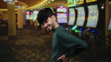 Kumar makineleriyle çevrili, parlak bir kumarhanede sırt ağrısı çeken genç bir adam, kapalı bir ortamda rahatsızlığını dile getiriyor..