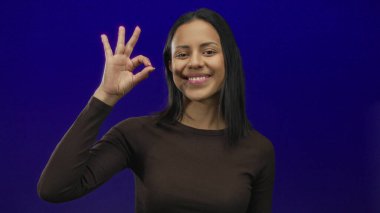 Gülümseyen ve el kol hareketi yapan bir kadın mavi bir arka plan duvarına yaslanmış genç ve anlamlı davranışlarını vurguluyor..