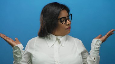 Beyaz gömlekli ve gözlüklü, iri yarı, İspanyol bir kadın, mavi duvarın üzerinde yüz ifadesiyle el ele tutuşuyor..