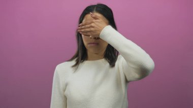 Pembe duvarın önünde yüzünü kapatan bir kadın stüdyo ortamında duygu ve yalnızlık gösteriyor.