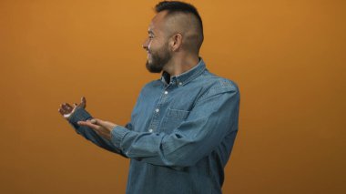 Turuncu stüdyoda kot gömlek giyerken ellerini açıp gülümseyen bir adam sıcaklığı ve arkadaşlığı hoş karşılar..