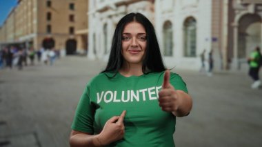 Gönüllü genç bir kadın kalabalık bir şehir caddesinde yeşil tişört giyip, gönüllü olarak yazılmış, pozitifliğini ve toplum ruhunu şehir ortamında aktarıyor..