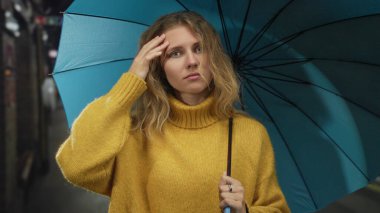 Kadın metroda şemsiyeyi endişeyle tutarken, mavi kazaklı sarışın genç manken şehir ortamında bir portre için poz veriyor..