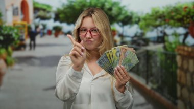 Bir şehir caddesinde elinde Romen banknotları tutan genç bir kadın bir gülümsemeyle kendinden emin bir şekilde öne bakıyor..