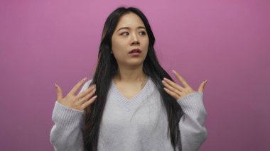 Kadın duygularını pembe arka plana karşı elleri ile ifade eder süveter giyer stüdyo ortamında uzun saçlarını göstererek samimi ve doğal anları yakalar.