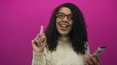Kadın, ekranda kaşlarını çatarken parlak pembe arkaplan ile akıllı telefonu stüdyoda tutarken kafasını kaşıyor..