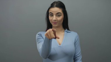 Mavi gömlekli İspanyol kadın gri duvara karşı kameraya doğru hareketler yapıyor. Kendine güvenen bir bakışla, bir bağlantı ve nişan anı yakalıyor..