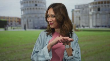 İspanyol kadın, Avrupa 'nın ünlü bir şehir simgesi olan Pisa, İtalya' daki ikonik eğik kulenin önünde para jesti yapıyor..