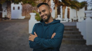 Kolları çapraz ve elleri görünür bir adam beyaz bina önünde kapüşonlu giyen merdivenler ve saksılar ile güven dostluğu.