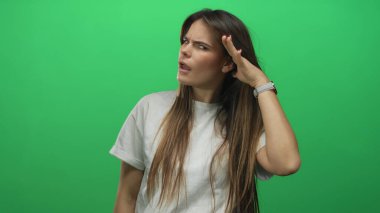 Beyaz gömlekli genç İspanyol kadın, izole edilmiş yeşil bir arka plan duvarına karşı dikkatle dinliyormuş gibi hareketler yapıyor..