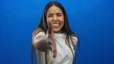 Gülümseyen ve el sıkışan bir kadın canlı mavi arka planda izole edilmiş. Stüdyo ortamında dostane bir hoş geldin davranışı izlenimi veriyor.