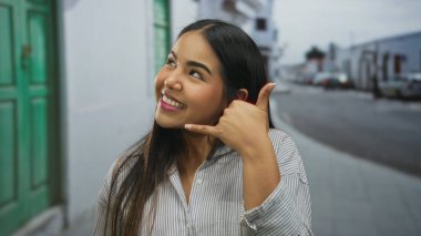 Sokak ortasında genç Latin kökenli Latin havası olan ve şehir zemininde gülümseyen bir kadın el sallıyor..