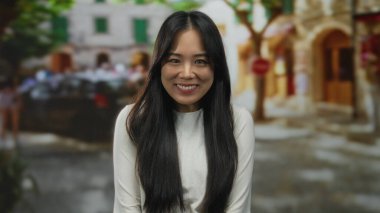 Çekici bir sokak ortamında gülümseyen genç Çinli kadın bulanık şehir manzarası ve arka plandaki insanlar canlı bir şehir atmosferini öneriyor..