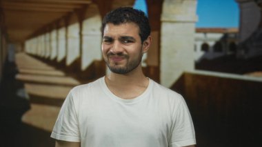 Sütunların altındaki tarihi bina koridorunda beyaz tişörtlü, ağzı ağızla kaplayan İspanyol genç adam iğrenme..