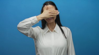 Beyaz tişörtlü İspanyol kadın gözlerini eliyle kapatıyor. Mavi duvarlı arka plandaki ifadeyi ortaya çıkarıyor..