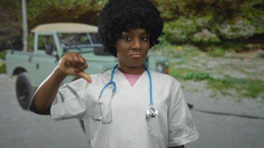 Ormanda steteskoplu genç bir kadın doktor baş parmağını kaldırıyor ve kaşlarını çatıyor; profesyonel olarak onaylamıyor..