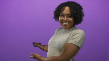 Avuç içleri açık, gülümseyen parlak bir kadın parlak mor bir stüdyoda el kol geziyor. Mutluluk..