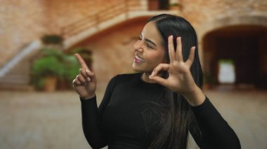Manzaralı arka planı olan eski bir kasabada mutlu bir şekilde el kol hareketi yapan kadın, pozitiflik ve neşe ifade ediyor, şehir dışında gezmek ve kültürel temalar için ideal..