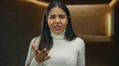 Salon ortamında belirsizlik ve tefekkürün göstergesi olarak tarafsız bir arka planda kafa karışıklığını ifade eden genç bir kadın..