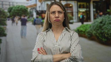 Bulanık mağazalar arasında, şehir alışveriş bölgesinde kolları çapraz olan çizgili gömlek ve gözlüklü kadın; reddedilme.