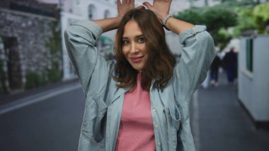 Genç İspanyol kadın açık havada şakacı poz veriyor. Sıradan bir kot ve pembe gömlek giyiyor. Hoş bir gülümsemesi ve enerjik bir enerjisi var..