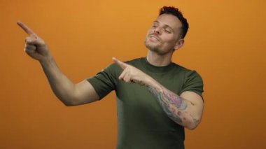 Genç adam gülümsüyor ve izole edilmiş turuncu bir arka planda dövmeli bir kolla pozitif ve çekici bir tavır sergiliyor..