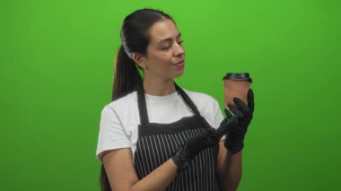 Çizgili önlüklü kadın yeşil stüdyoda eldiven takmış kahve fincanı tutuyor..