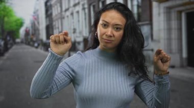 Kadın, mavi süveter ve halka küpe takan bir şehir caddesini işaret ediyor..