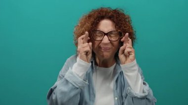 Kıvırcık saçlı ve gözlüklü bir kadın yeşil arka plan duvarına yaslanmış umut ve heyecanı ifade ediyor..