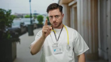 Doktor, şehir sokağında ciddi bir ifadeyle işaret ediyor. Steteskoplu genç adam dışarıda bekliyor..