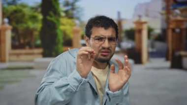 Kot ceketli ve gözlüklü genç İspanyol adam şehir caddesindeki çerçeveleri ayarlarken elleriyle yüzünü koruyor; gerginlikten korkuyor.