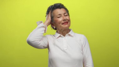 Gri saçlı, gülümseyen ve saçlarına dokunan son sınıf öğrencisi bir kadın hayat dolu sarı bir arka plana karşı, güven ve neşe taşıyor..