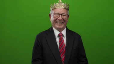 Takım elbiseli kıdemli bir adam yeşil bir arka plana esprili bir şekilde yan bakıyor, açık yürekli ve çekici bir tavır sergiliyor..