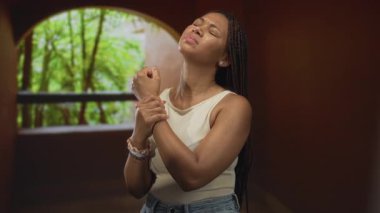 Kadın bileklerini kavrıyor ve bilekleriyle kemerli pencerenin yanındaki koridorda dikilirken ürküyor; acıyla ilgili..