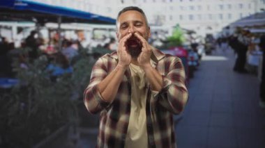 Sakallı ve gri fincanlı bir adam sokak terası restoranında bağırıyor. Dışarısı kalabalık. Acil çağrı..