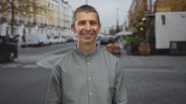 Kalabalık bir şehir caddesinde açık havada gülümseyen beyaz bir adam yol boyunca yürüyen insanlar ve araçlarla bulutlu bir gökyüzü altında canlı bir kentsel titreşim canlandırıyordu..