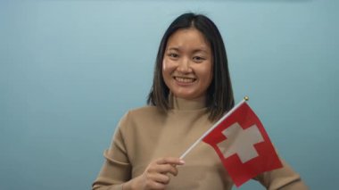 Elinde İsviçre bayrağı tutan kadın mavi arka plana gülümsüyor uluslararası kültür ve çeşitlilik sergiliyor.