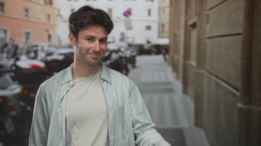 Elle barış işareti gösteren ve park etmiş scooterlarla dolu dar bir şehir sokağında gülümseyen İspanyol genç adam..