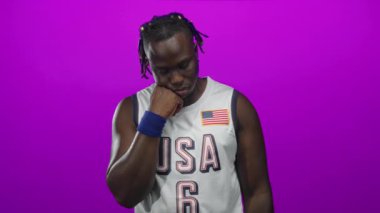 Elleri çenesinde ABD basketbol forması ve mavi bileklik takan, mor bantlı Amerikan bayrağı takan adam..