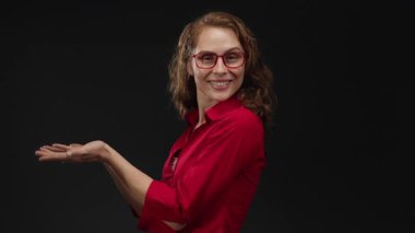 Kırmızı gömlekli bir kadın siyah bir arka plan üzerinde kollarını açmış gülümsüyor, bir tanışma ve nişan hissi veriyor..