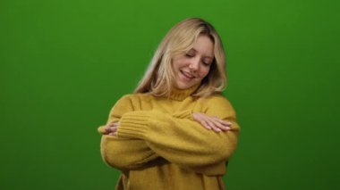 Sıcak sarı bir kazak içinde gülümseyen bir kadın canlı yeşil bir duvara sarılıyor. Yumuşak ifadesi ve rahat duruşu sayesinde sıcaklığını ve rahatlığını yayıyor..