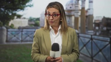 Sokak sahnesi önünde elleri ve kırmızı gözlükleriyle mikrofon tutan kadın muhabir; basın şüpheciliği.