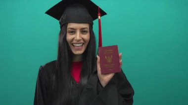 Graduated young woman in cap and gown holding thailand passport against green background, signifying achievement and international prospects.