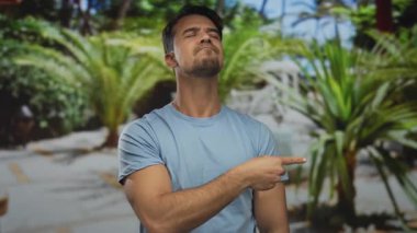 Parktaki genç İspanyol adam, kendine güveni olan, yemyeşil yeşillik ve doğa manzarasıyla çevrili bir ifadeyle dikkatsizce işaret ediyor..