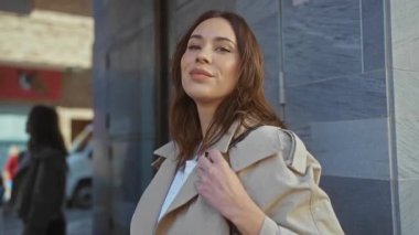 Gündüz vakti şehir mimarisi ile çevrili bir caddede güvenle gülümseyen genç İspanyol kadın..