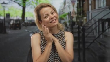 Genç sarışın kadın ellerini yanağına yapıştırıyor ve bir şehir caddesinde geniş bir gülümseme; memnuniyet.
