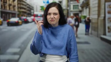 Duygularını ifade eden kadın, hareket halindeki insan ve araçların bulanık arka planına sahip kalabalık şehir sokak ortamına baş aşağı bir jest yapıyor..