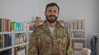 Askeri üniformalı İspanyol bir adam, gönüllü bir odada raflarda erzak ve paketlerle duruyor. Yardım çabalarını öneriyor.
