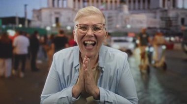 Elleri sımsıkı bağlı bir kadın, kalabalık bir sokak kalabalığının arasında gülüyor ve gülüyor, scooterları ve arabaları aydınlık bir binanın yakınında; sevinç kutlamaları.